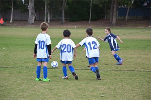 Four very young kids all going for the ball during a game