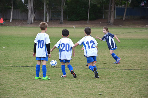 Four very young kids all going for the ball during a game