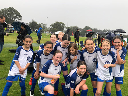 A young female team posing for a team photo after a game in the rain, they are all smiling and happy