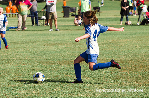 young girl with hair flying about to kick soccer ball during game