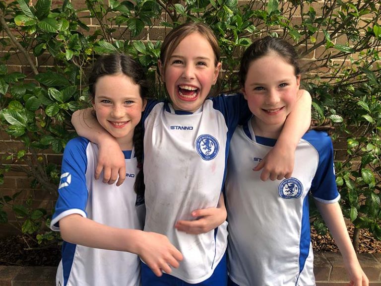 three young girls with big smiles wearing blue and white soccer uniforms with arms around each other